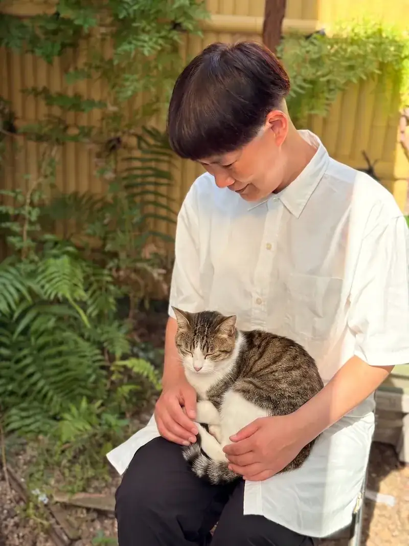 熊本・猫のお見送り代行 凪 代表 竹下夕子。庭先でやわらかな光の中、猫を膝に抱いています。